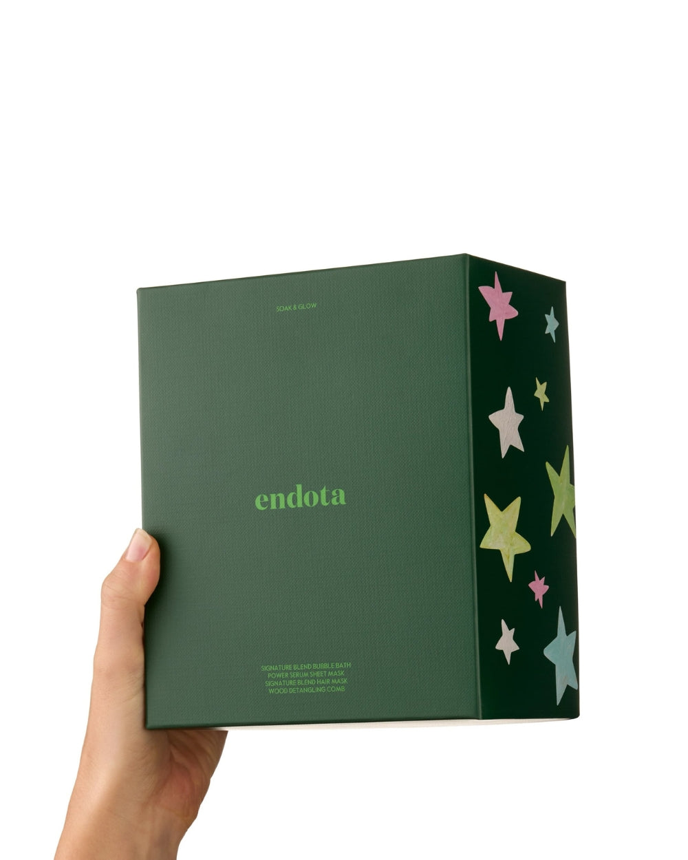 A hand holding a dark greenendota gift box with a side panel decorated with colourful pastel stars, set against a plain white background.
