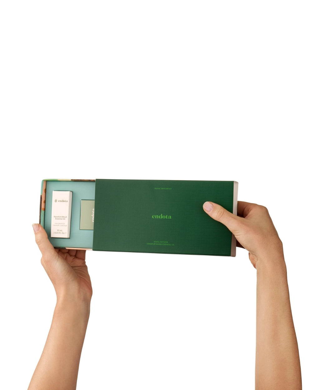 A person's hands holding open a green endota travel diffuser gift set box against a solid white background.