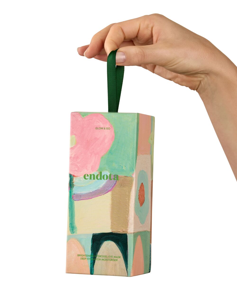 A hand holding a colorful abstract-patterned bon bon gift box with a dark green ribbon handle. The box features the brand name 'endota' and text for 'Go & Glow' gift pack.