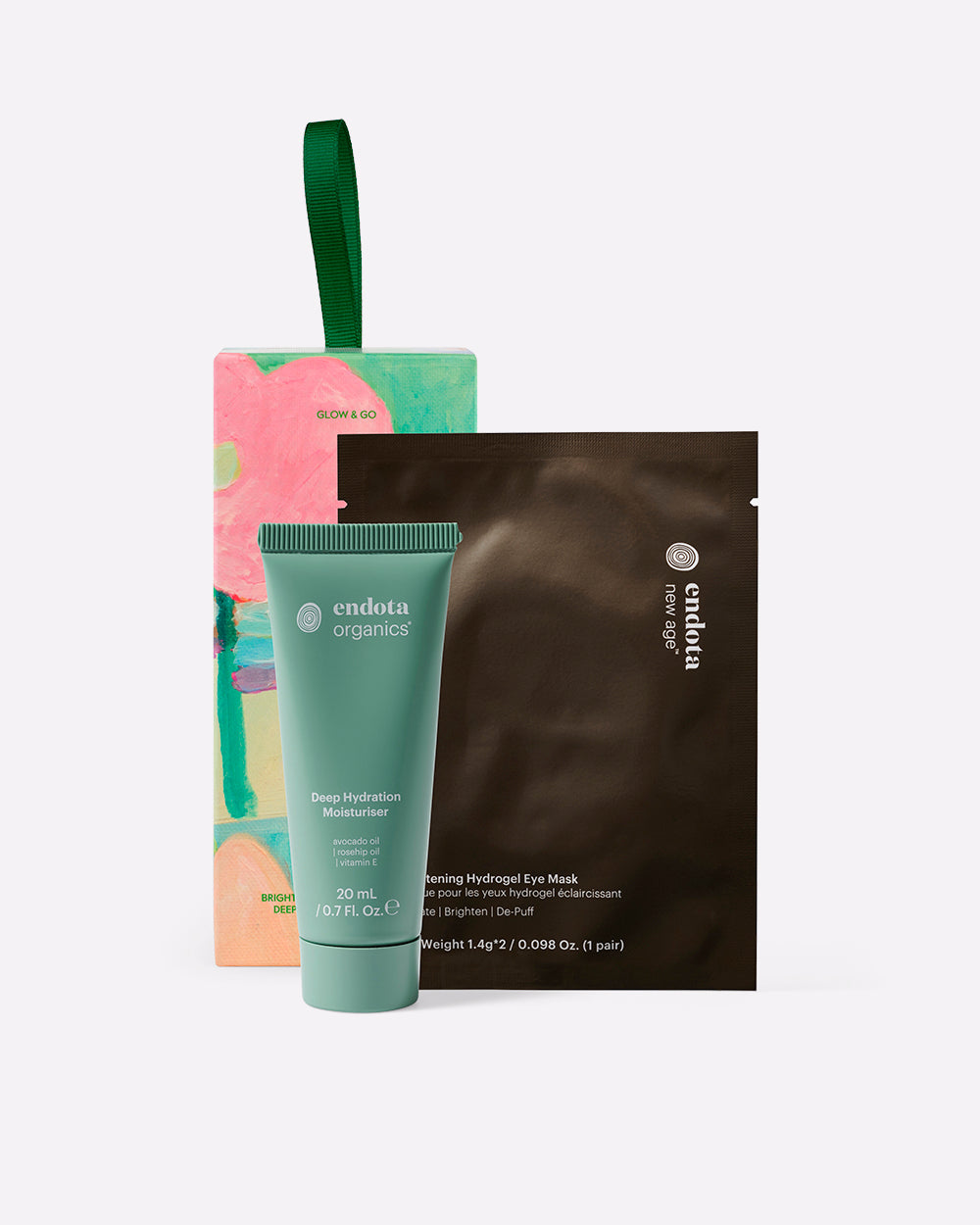 endota Organics skincare set featuring a green tube of Deep Hydration Moisturiser, a brown sheet mask packet, and a colorful bon bon gift box with a green handle, arranged on a light grey background.