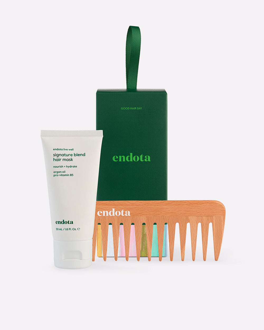 endota hair care gift set on a light grey background, featuring a white tube of signature blend hair mask, a dark green bon bon gift box with a green handle, and a wooden comb.