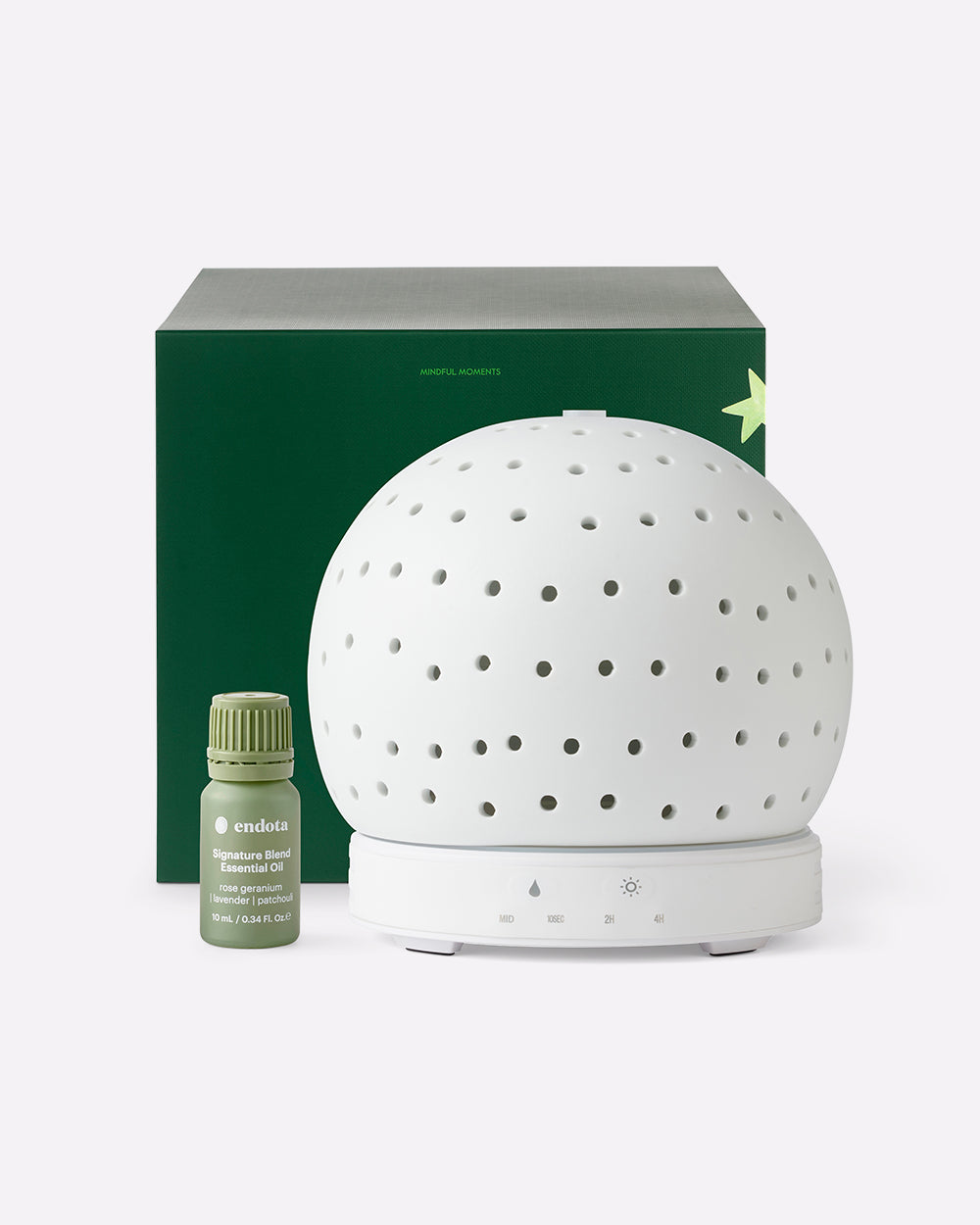 A white spherical ceramic diffuser with perforated holes on a white base, shown with a dark green gift box and a small green essential oil bottle on a light grey background.