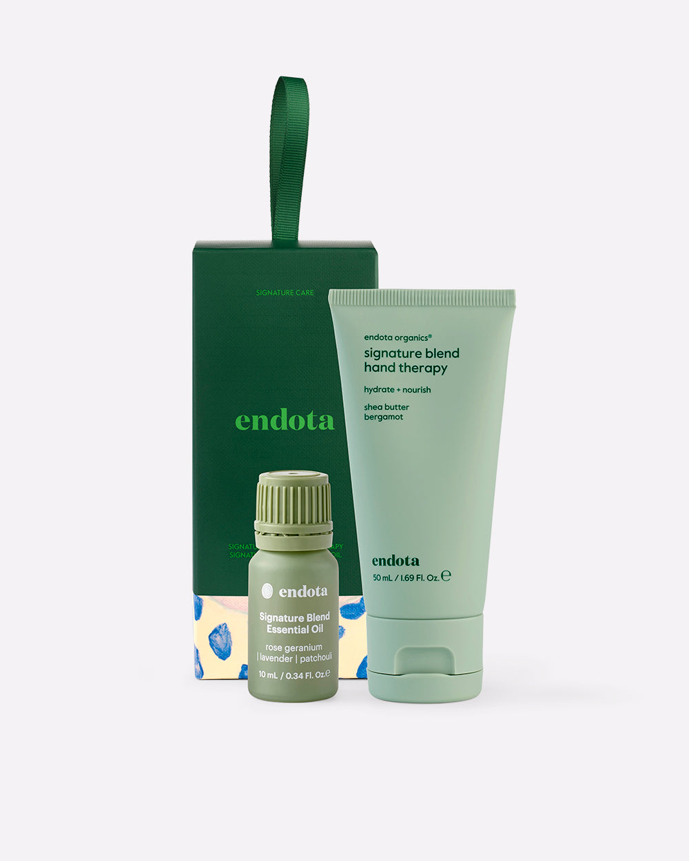 endota 'Signature Care' gift set featuring a light green hand therapy tube, a small green essential oil bottle, and a dark green bon bon gift box with a carrying loop, on a light grey background.