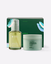 endota skincare set featuring a Signature Body & Massage Oil in a clear bottle with a pale green pump, a Coffee and Sea Salt Body Polish in a pale mint green jar, and the dark green branded gift box behind them, on a light grey background.
