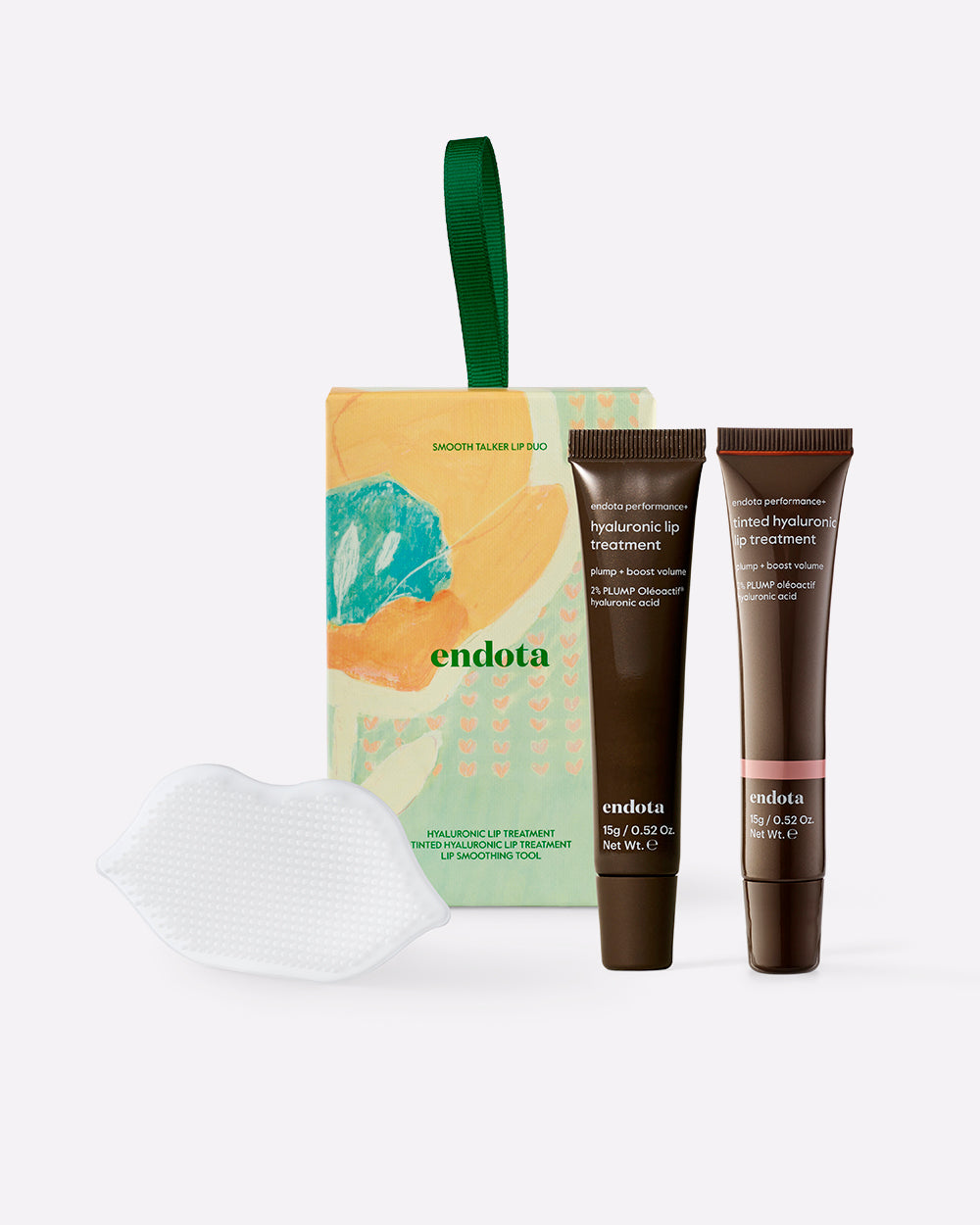 endota hyaluronic lip care set featuring a gift box with a green handle, two dark brown tubes of Hyaluronic Lip Treatment, and a white textured lip exfoliator on a light grey background.