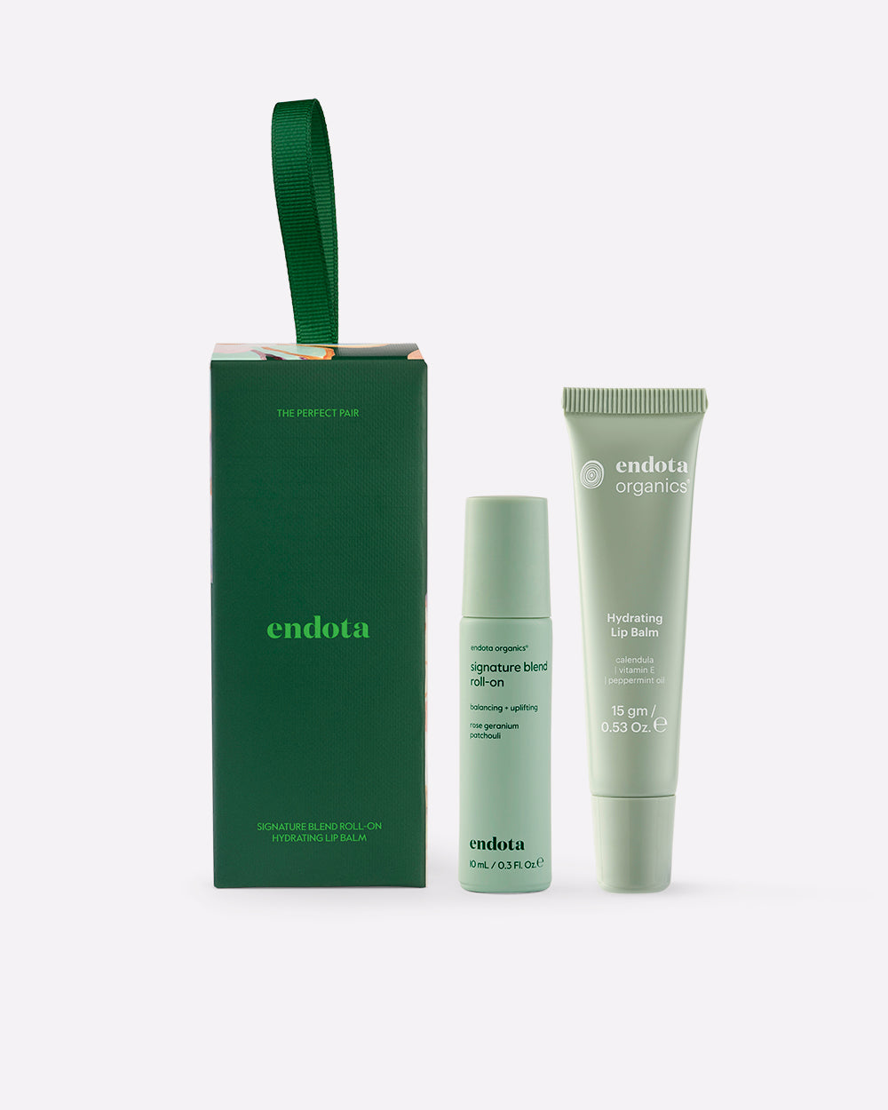 endota gift set featuring a green gift box with a green ribbon handle, a signature blend roll-on bottle, and a hydrating lip balm tube, all in a light sage green color, on a light grey background.