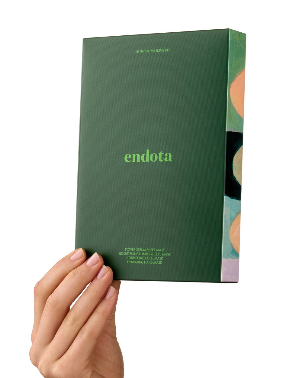A hand holding a dark green endota mask gift set box against a clean white background. The box features the brand name 'endota' in light green text and has a side panel with abstract circular patterns in peach, black, and light purple.
