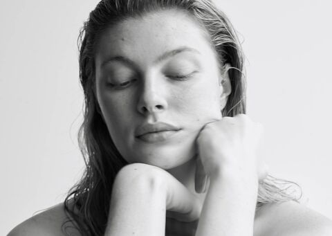Black and white close-up portrait of a woman looking down with her hand on her face against a plain background
