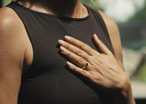 Close-up of a person wearing a black sleeveless top with a hand on their chest.