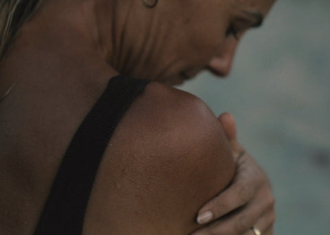 Close-up of a person's face holding their shoulder and looking down with a blurred background