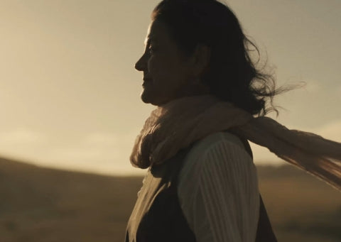 Person with a scarf standing in a field landscape at sunset